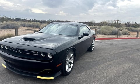 Black Dodge Challenger muscle car parked in lot with yellow bumper accents and desert landscape background