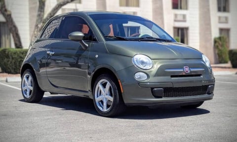 Gray Fiat 500 compact car parked on street with residential building in background