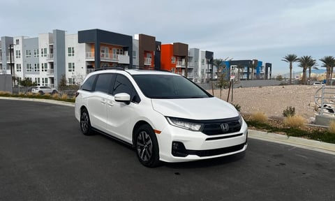 White Honda minivan parked on a residential street with modern apartment buildings and palm trees in the background