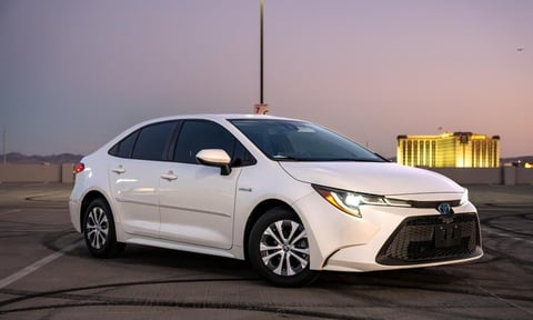 White Toyota Corolla sedan parked on empty parking lot at dusk with industrial building in background
