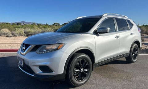 White Nissan Rogue SUV parked on a desert road with clear blue sky and sandy landscape in background