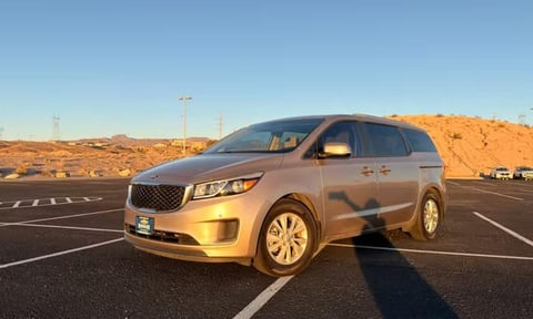 Gold-colored minivan parked in empty lot with desert hills and blue sky in background