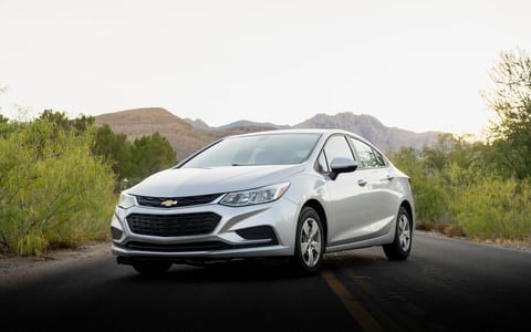 White Chevrolet Cruze sedan parked on a desert road with mountains and vegetation in the background