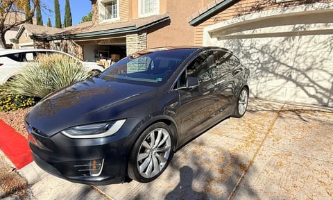 Black Tesla Model X parked in a residential driveway with a garage and landscaping visible