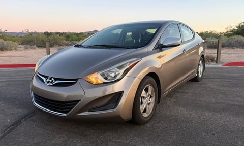 Silver Hyundai Elantra sedan parked in lot with desert landscape and red barrier visible in background