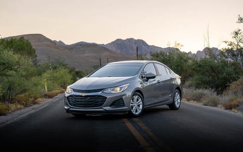 Blue Chevrolet sedan parked on desert highway with mountain range and desert vegetation in background