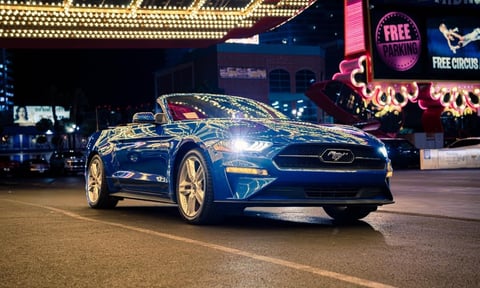 Blue Ford Mustang convertible parked on a nighttime Las Vegas street with illuminated casino signs in the background