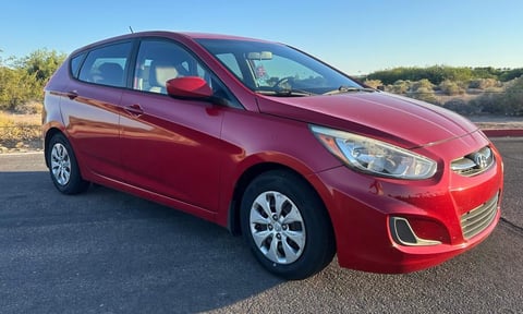 Red Hyundai Accent hatchback car parked on asphalt with desert landscape in background