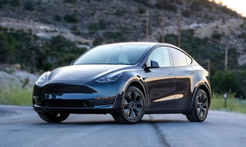 Black Tesla electric vehicle parked on road with rocky hillside in background