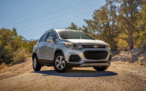 Silver Chevrolet Trax compact SUV parked on a dirt road surrounded by trees and dry brush